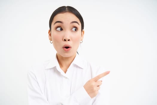 Smiling businesswoman, asian office manager pointing right, showing advertisement aside on empty copy space banner, standing over white background.