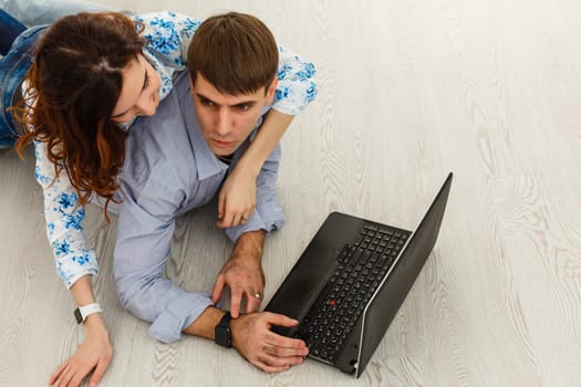 Couple Use Laptop Computer, while Sitting on the Living Floor room of their Apartment. Boyfriend and Girlfriend Talk, Shop on Internet, Choose Product to Order Online, Watch Streaming Service