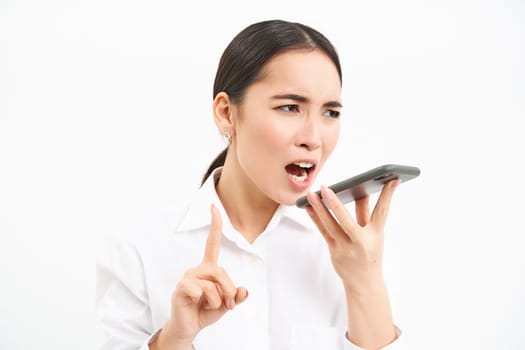Angry korean saleswoman, shouting at smartphone speaker, screaming at mobile phone, scolding employee on cellphone, white background.
