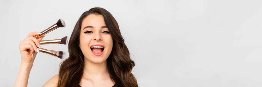 Young woman holding a set of makeup brushes with a surprised facial expression.