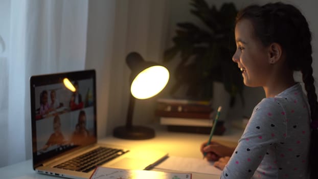 Pretty primary school girl distance learning at home. Focused cute kid listening audio lesson studying at table, doing homework. Children remote education on quarantine concept.