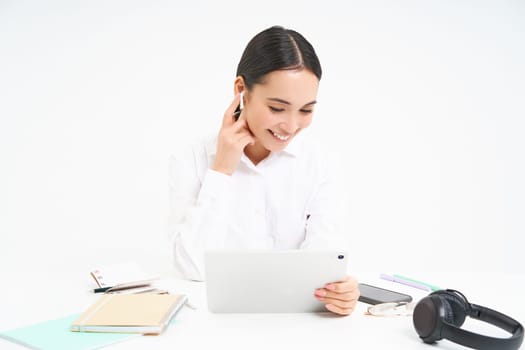 Portrait of korean businesswoman in headphones, connects to meeting on digital tablet, talks on video chat, joins online conference, white background.