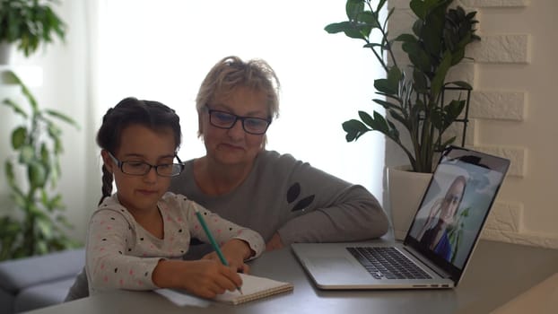 little girl studying with her grandmother at home, use laptop for education, online study, home studying. Girl has homework at distance learning. Lifestyle concept for Family quarantine covid-19.