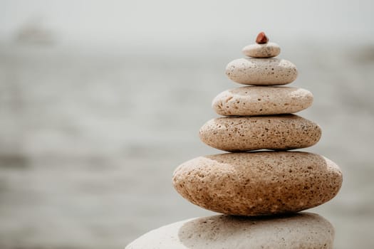 Pyramid stones on the seashore with warm sunset on the sea background. Happy holidays. Pebble beach, calm sea, travel destination. Concept of happy vacation on the sea, meditation, spa, calmness.