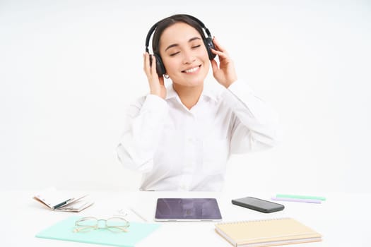 Smiling businesswoman in headphones, sits at office desk listens music and relaxes, rests after work, white background.