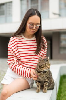 Young woman and tabby cat sitting on a bench outdoors