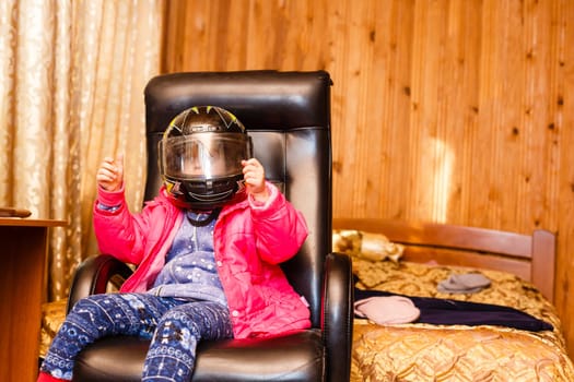 little girl in a motorcycle helmet in a chair at home.