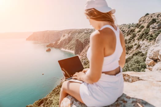 Digital nomad, Business woman working on laptop by the sea. Pretty lady typing on computer by the sea at sunset, makes a business transaction online from a distance. Freelance remote work on vacation