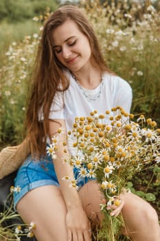 Beautiful young woman in nature with a bouquet of daisies. Field daisies, field of flowers. Summer tender photo.