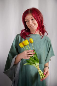 Beautiful woman with red hair in yellow dress on light background holds tulips. Inernational woman's day 8 March