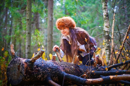 Girl in a leather jacket, a big red fox fur hat in the forest in autumn. A female model poses as a fabulous royal huntress on nature hunt at a photo shoot