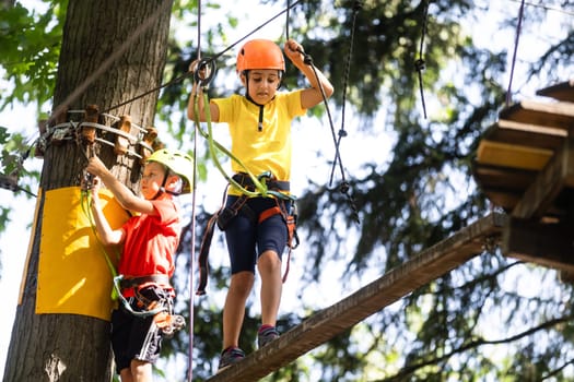 Child in forest adventure park. Kids climb on high rope trail. Agility and climbing outdoor amusement center for children. Little girl playing outdoors. School yard playground with rope way