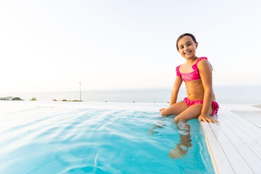 Little girl playing in outdoor swimming pool jumping into water on summer vacation on tropical beach island. Child learning to swim in outdoor pool of luxury resort.