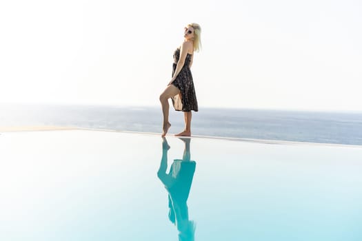 An attractive young woman stands near the pool with a panoramic view.