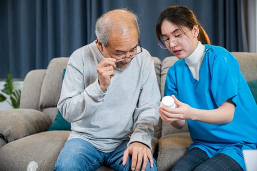 Asian nurse with physician explaining prescription medicine to attentive senior man at home, Doctor woman explain dosage pill old man, Healthcare worker caregiver visiting in house in living room