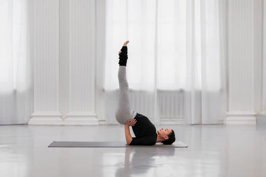Professional instructor young woman does sarvangasana during a yoga class in a white light studio. The concept of getting rid of any ailment from allergies to nervous tension.