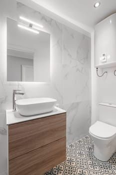 Close-up of an empty bathroom in white tones with a sink with a cabinet and a mirror and a toilet bowl in a new apartment. Stylish Scandinavian design concept.