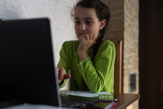 Smiling little Caucasian girl in headphones have video call distant class with teacher using laptop, happy small child wave greeting with tutor, study online on computer, homeschooling concept.