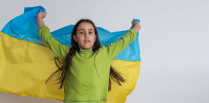 Child carries fluttering blue and yellow flag of Ukraine isolated on white. Ukraine's Independence Day. Flag Day. Constitution day. Girl in traditional embroidery with flag of Ukraine.