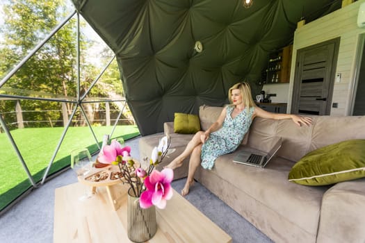 middle aged woman uses a laptop resting and spending time at Glamping house on holidays. holiday dome tent. Cozy, camping, hygge, lifestyle concept.