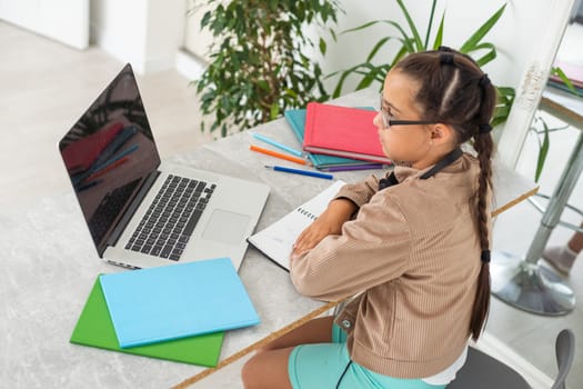Portrait of smart schoolgirl sitting in classroom and typing.