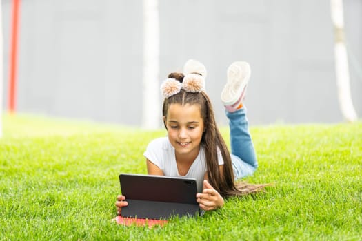 Little girl sitting on grass and playing tablet pc.