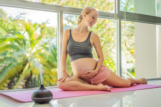 Young pregnant woman doing yoga exercises and meditating at home with an aroma diffuser. Health care, mindfulness, relaxation and wellness concept. Aromatherapy during pregnancy.