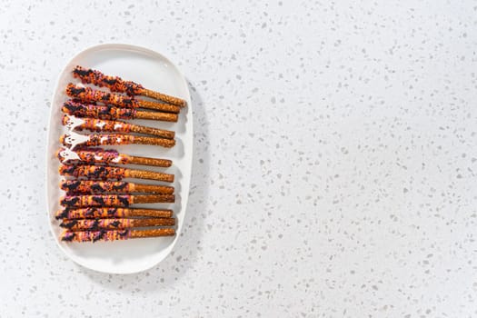 Flat lay. Halloween chocolate-covered pretzel rods with sprinkles on a white serving plate.