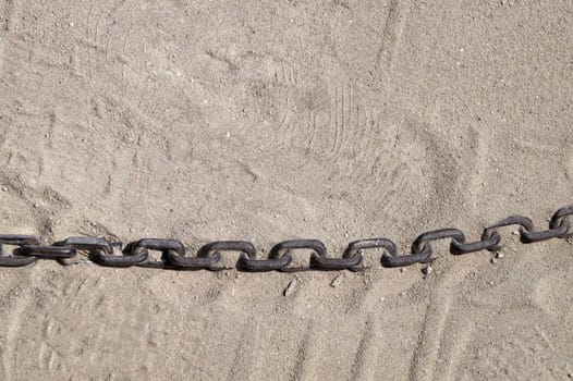 old rusty metal chain on sand in sunlight, copy space.