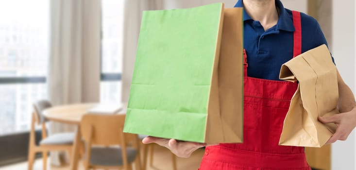 Young handsome delivery man holding paper bag with takeaway food happy with big smile