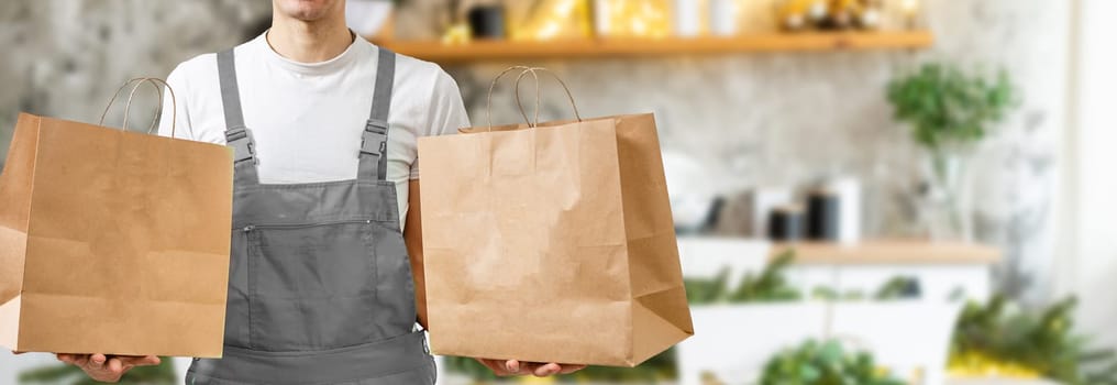 Courier holding paper bags with food, space for text. Delivery service.