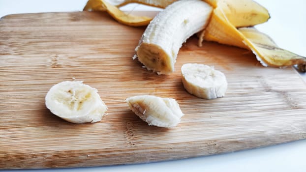 Banana with open panel and sliced round pieces on wooden board and white background. Ripe banana with peel cooking, Close up. Delicious sweet fruit dessert