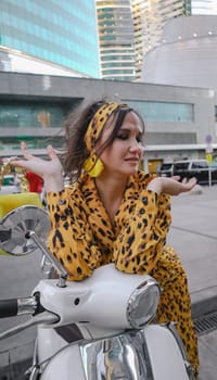 A portrait of a fashion-dressed happy woman posing for a photo shoot on a moped