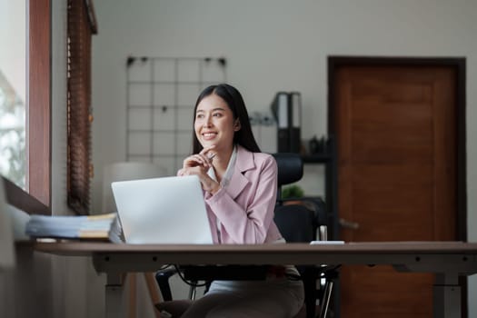 Portrait of a woman business owner showing a happy smiling face as he has successfully invested her business using computers and financial budget documents at work.