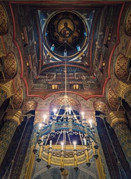 Interior architectural details of the Curtea de Arges monastery. The hall with tall columns, christian Orthodox painted icons on walls and a golden chandelier with lights suspend out of ceiling