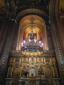 Interior details of Curtea de Arges monastery. The altar and ornate walls with painted icons and a golden chandelier with lights suspending out of ceiling