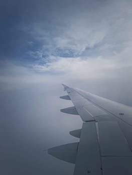 Plane flight through the dense foggy clouds, vertical shot. Airplane wing seen through the window
