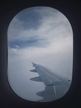 Plane flight through the dense foggy clouds. Airplane wing seen through the window