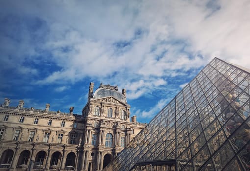 Outdoors view to the Louvre Museum in Paris, France. The historical palace building with the modern glass pyramid in center