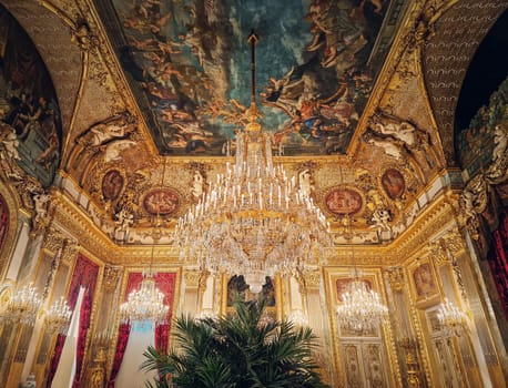 Beautiful decorated Napoleon apartments at Louvre palace. Royal family rooms with cardinal red curtains, golden ornate walls, paintings and crystal chandeliers suspended from ceiling