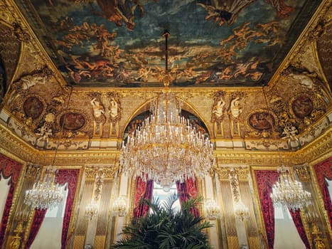 Beautiful decorated Napoleon apartments at Louvre palace. Royal family rooms with cardinal red curtains, golden ornate walls, paintings and crystal chandeliers suspended from ceiling