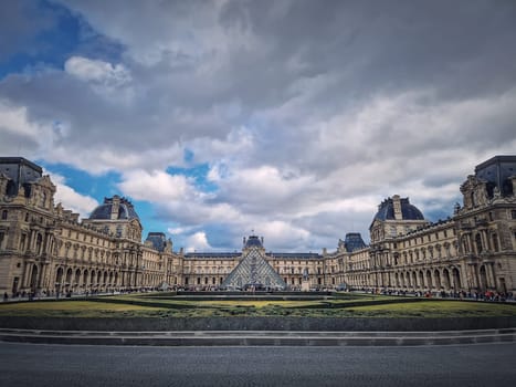 Outdoors view to the Louvre Museum in Paris, France. The historical palace building with the modern glass pyramid in center