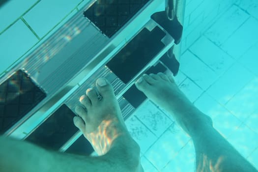 Underwater photo, man feet stepping on pool stairs.
