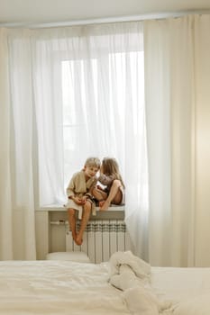 A boy and a girl in bathrobes are sitting on the windowsill, talking, playing.