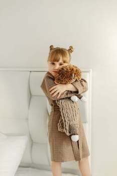 A girl in a dressing gown plays with a knitted hedgehog in the room.