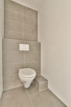 a white toilet in the corner of a room with grey tiles on the walls and floor, there is no one to be seen