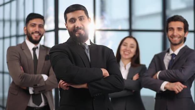 Smiling leader ceo or professional business coach looking at camera posing in office with diverse happy team at background,
