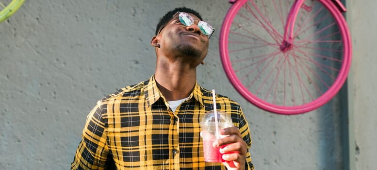 Young cheerful african american male on city having fun and holding cocktail. Man on summer holiday. Leisure lifestyle holiday and summer drinks concept.
