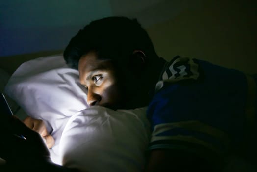 young man sitting on bed using smart phone at night .