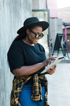 Beautiful African American woman using digital tablet, watching movie outdoors. Successful blogger influencer streaming video, communication online